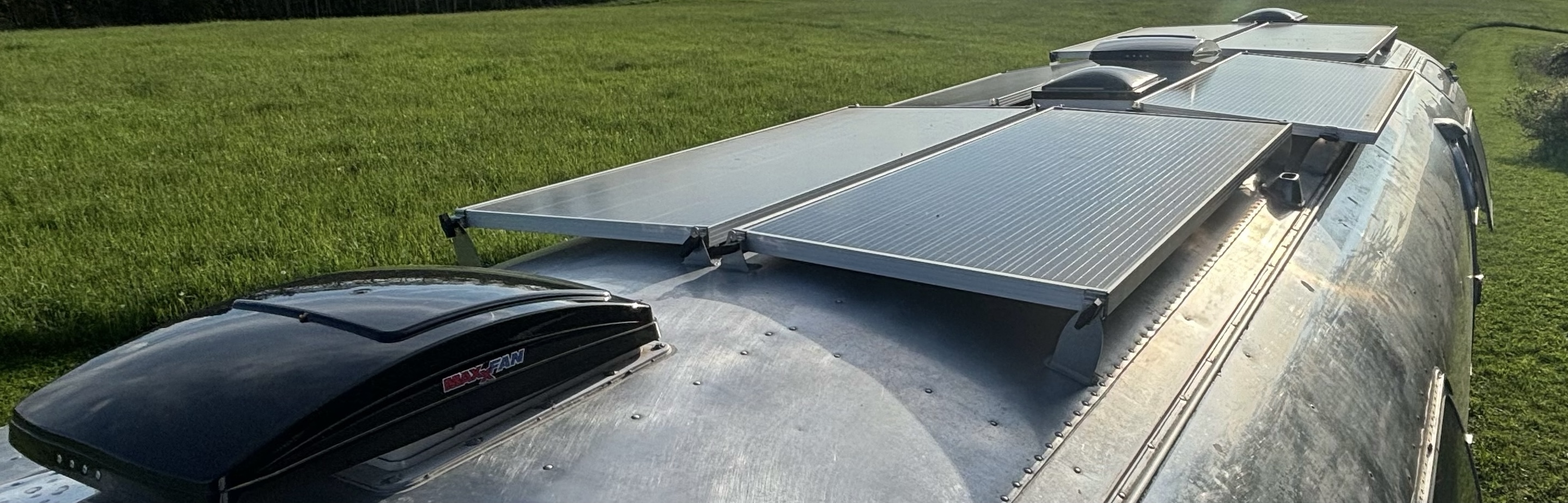 Solar panels mounted on the roof of an aluminum Airstream trailer parked on grass